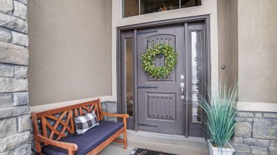 Gray entry door with a green wreath and bench in front of it